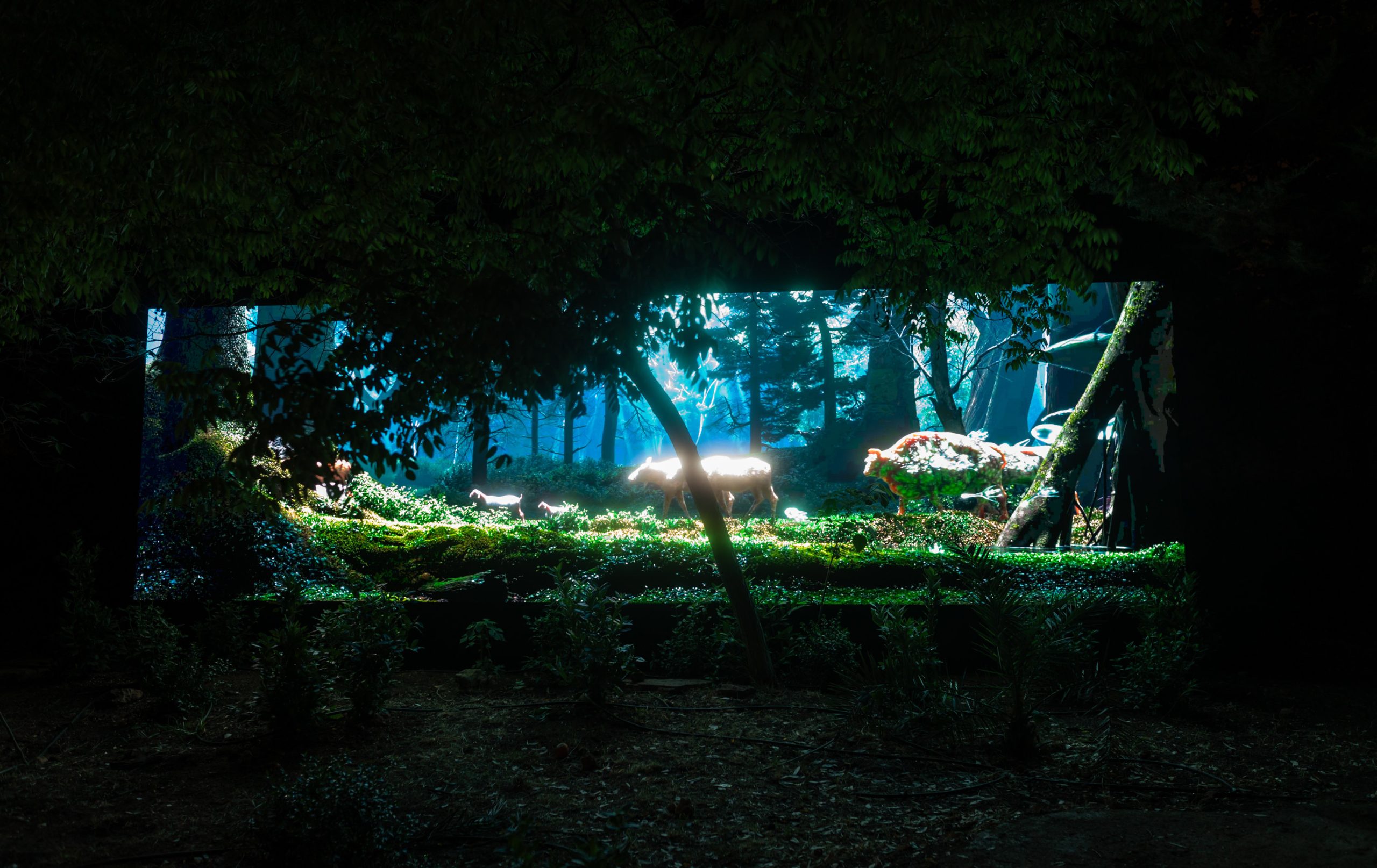 Aias Kokkalis - Ares Awakening - A large, illuminated display shows a CGI forest scene with various animals, including a deer, surrounded by trees and greenery, set against the darkness of an outdoor environment at night.